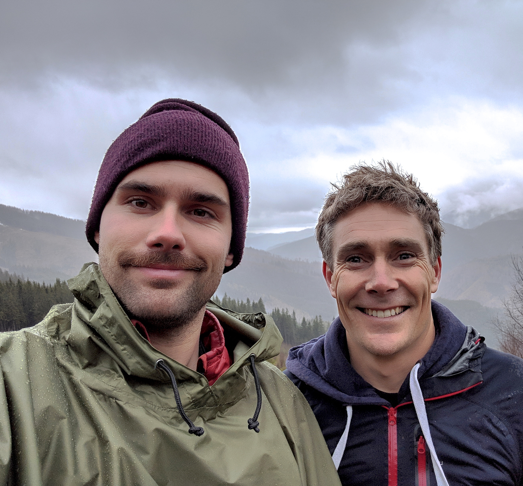 The two co-founders smiling with hilly forests in the background